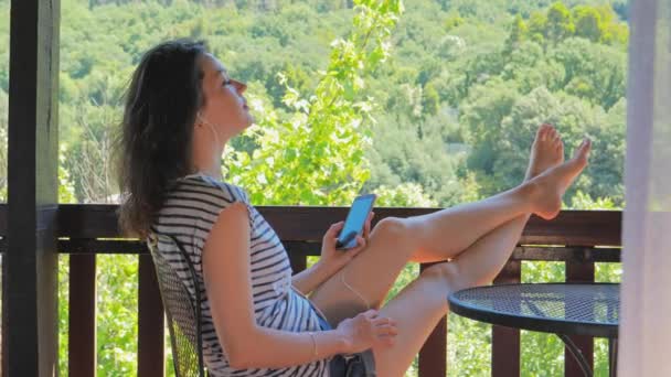 Νεαρή γυναίκα στο μπαλκόνι να ακούει μουσική ή να μιλάει τηλεφωνικώς — Αρχείο Βίντεο