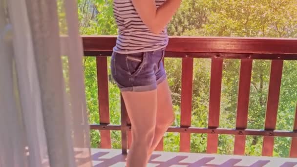 Junge tanzende Frau auf einem Balkon, die per Telefon Musik hört — Stockvideo