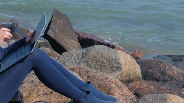 Mujer sentada en la costa del mar y usando laptop . — Vídeos de Stock