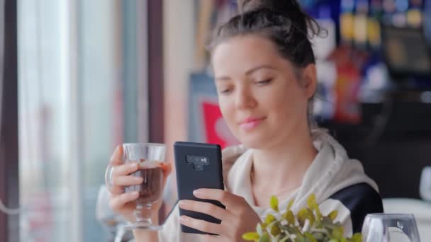 Mulher bonita com xícara de mensagens de texto de chocolate quente com seu celular no café — Vídeo de Stock