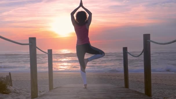 Mujer practicando yoga en paseos por la playa de madera, hermosa puesta de sol en verano. — Vídeo de stock