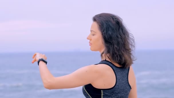 Жінка біжить на березі моря, дивлячись дані на фітнес-годинник — стокове відео