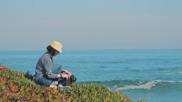 Vrouw met strohoed gaat laptop gebruiken op mooie kustlijn — Stockvideo