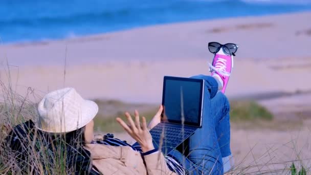 Femme allongée sur le sable et bavardant en ligne avec ses amis sur la plage — Video