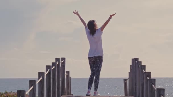 Mujer feliz con los brazos en la orilla del océano pasarela de madera — Vídeos de Stock