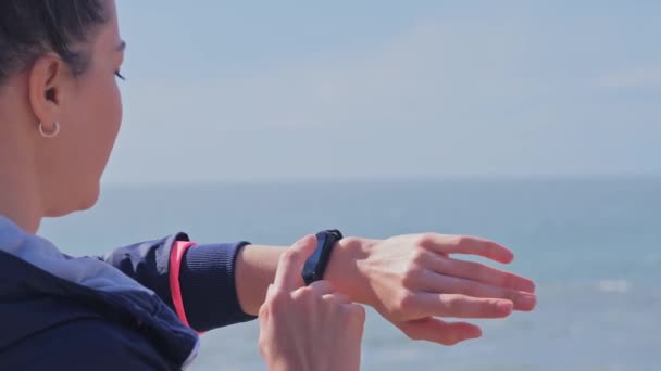 Woman looking at her smartwatch during workout at beach — Stock Video