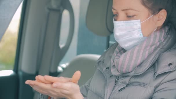 Vrouw in auto met chirurgisch masker op gezicht desinfecterende handen. COVID-19 Coronavirus — Stockvideo