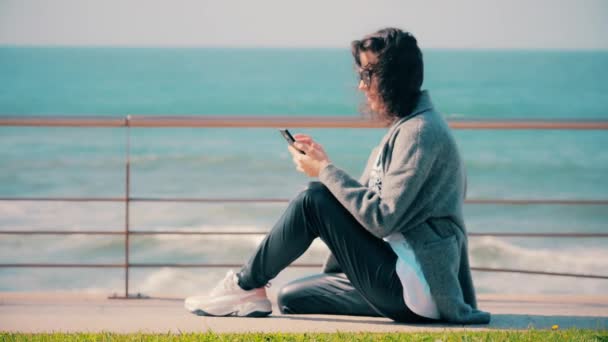 Μελαχρινή κοπέλα που διαβάζει ή γράφει sms στο κινητό της smartphone. — Αρχείο Βίντεο