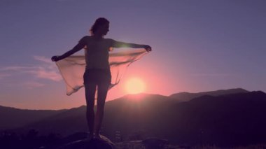 Elleri havada, rüzgarda eşarp tutan genç bir kadın.