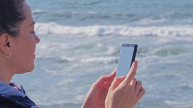 Kumsalda cep telefonunda sohbet mesajı yazan esmer kadın.