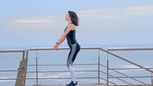 Ajuste mujer fuerte en ropa deportiva haciendo ejercicio en cuclillas en la orilla del mar — Vídeo de stock