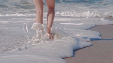 Okyanusun köpüklü dalgalarıyla kumsalda yürüyen bir kadın..