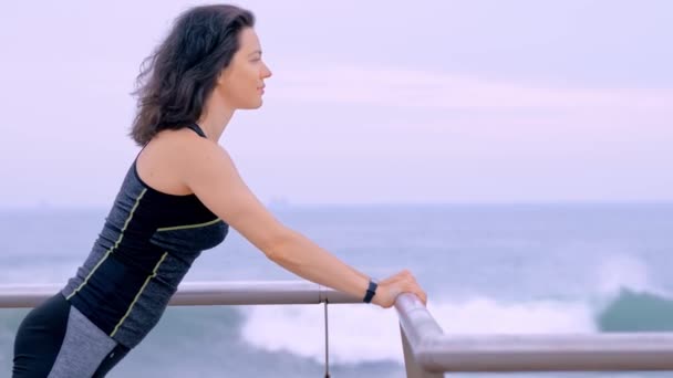 Deniz kıyısında spor kıyafetleri içinde spor egzersizleri yapan aktif bir kadın. — Stok video