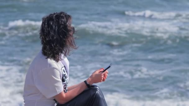 Donna rilassante e godendo mattina d'estate sulla spiaggia tenendo il suo smartphone . — Video Stock