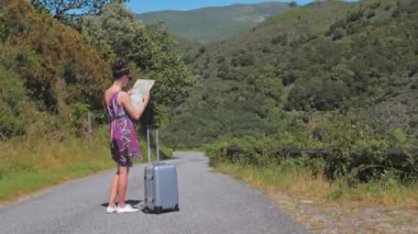 Kadın bir bavulla seyahat eder, elinde haritayla yolculuklarını planlar.