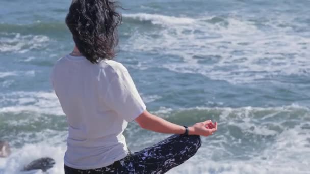 Женщина медитирует в позе лотоса на скалах на берегу моря — стоковое видео