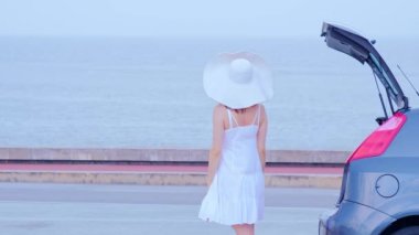 Büyük yaz şapkalı kadın arabayla seyahat eder, deniz kenarında ellerini kaldırır.