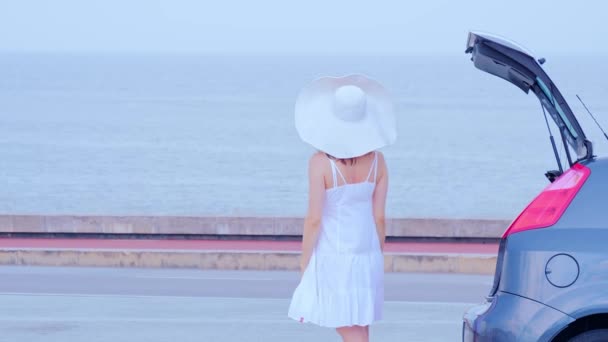 Женщина в большой летней шляпе едет на машине, поднимает руки на берегу моря — стоковое видео