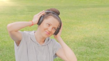 Güzel bir kadın çimlere uzanıp müzik dinliyor.