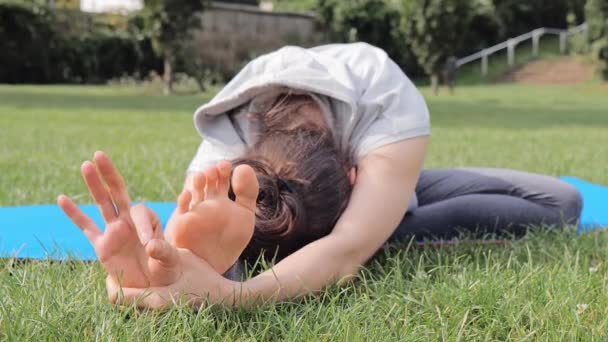 Молодая женщина практикует упражнения йоги на зеленой траве — стоковое видео