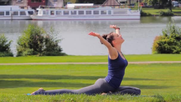 Девушка практикует йогу голубя асана в парке — стоковое видео