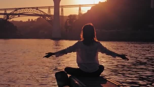 Nilüfer pozisyonunda meditasyon yapan kadın, gün batımında Porto 'nun ünlü köprüleri. — Stok video