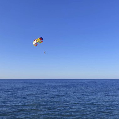 Paraşütlü bir adam denizin üzerinde uçuyor..