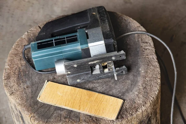 一个带有锋利锯子和层压板的电锯躺在木刻上 电锯用于在安装过程中切割层压板 车间中的细木工和家庭工匠的电动工具 — 图库照片