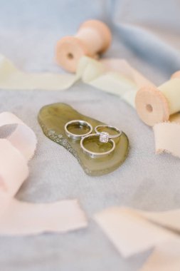 Elmas yüzükler ve alyanslar. Gri arkaplanda ve çiçeğin önünde.