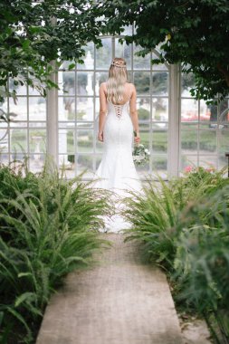 Gelin sırtı dönük poz veriyor. Elinde bir gelin çiçeği var..