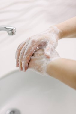 Kadın ellerini cerrahi el yıkama yöntemiyle yıkıyor. En az 20 saniye ellerini yıkıyor. Parmaklarıyla elleri arasında yıkanır. Covid-19 'dan korunmak için ellerini yıkıyor..