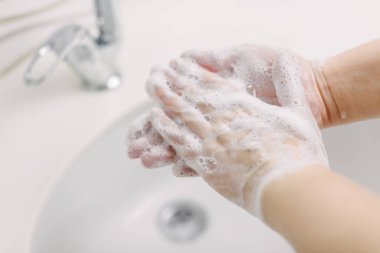 Kadın ellerini cerrahi el yıkama yöntemiyle yıkıyor. En az 20 saniye ellerini yıkıyor. O, onun elinin avuç içini ovalıyor. Covid-19 'dan korunmak için ellerini yıkıyor..