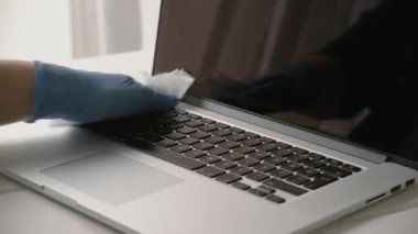 Kadın onu koronavirüsten korumak için bilgisayarının klavyesini temizliyor. Temizlik bezini ve eldiveni kullanıyor..