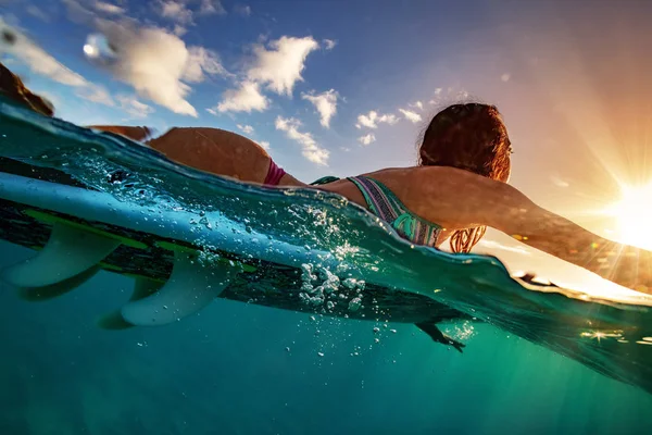 Surfista menina remando em uma placa ao pôr do sol — Fotografia de Stock