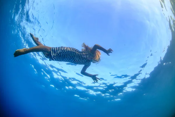 可爱的孩子一个金发碧眼的小女孩穿着海上剥去的衬衫游泳在海水水下拍摄蓝色背景 — 图库照片