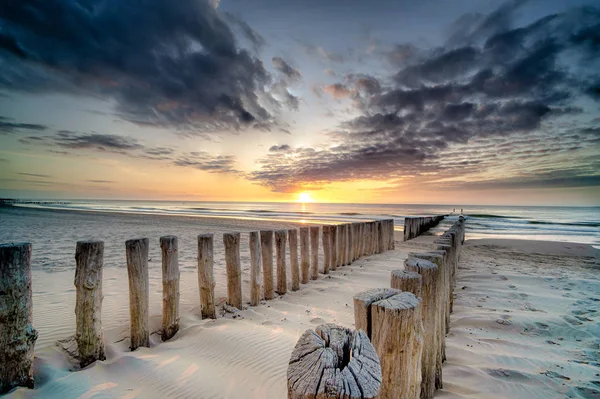 Groyne 'lar ve dalga kırıcılar gün batımından hemen önce sakin bir denizde 