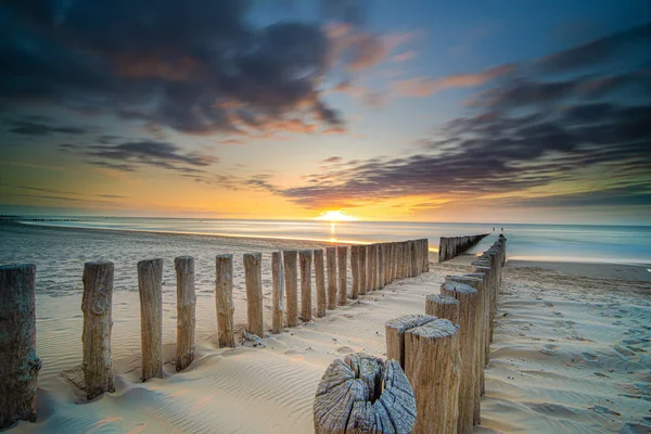 Groyne 'lar ve dalga kırıcılar gün batımından hemen önce sakin bir denizde 