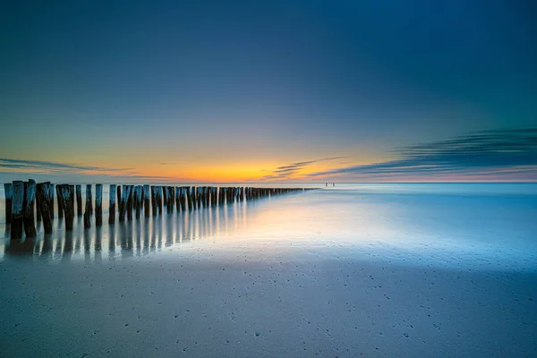 Groynes e disjuntores de onda em um mar liso pouco antes do pôr do sol em — Fotografia de Stock