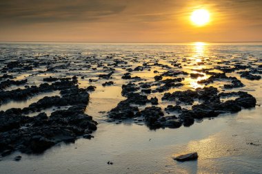 'Dalgalar çekildiğinde' çamurlu düz 'manzaralı dramatik günbatımı gökyüzü altında bulutlarla