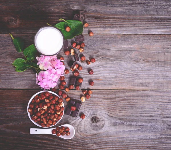 Frische Haselnüsse, Milch und dunkle Schokolade auf Holztisch — Stockfoto