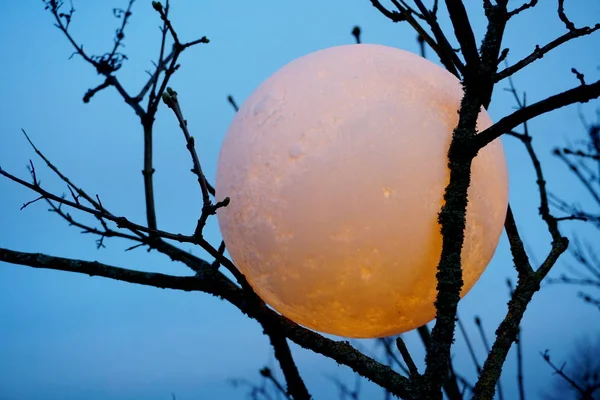 Round full moon in hands against evening sky. Lunar model, moon-shaped lamp with moon craters