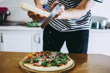 Şef çiğ pizza hamurunun üzerine parmesanlı peynir sürüyor.