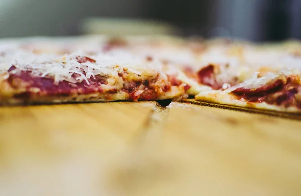 Primer plano de pizza casera con salami y rodaja de grana padano colocada en la plancha de madera. Fondo borroso — Foto de Stock