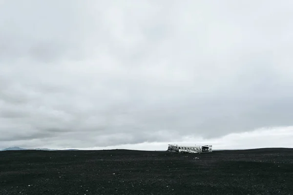 O avião destruído abandonado no meio da areia negra na Islândia. Céu de nuvem cinza . — Fotografia de Stock