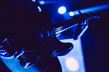 Gösteri sırasında koyu mavi sahne ışığında bir gitarın yakın çekimi.