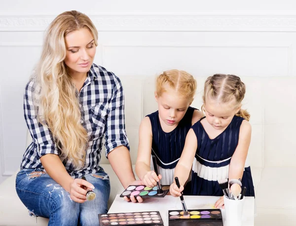 Joven madre con dos hermosas hijas con una paleta de maquillaje — Foto de Stock