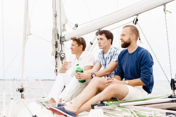 Счастливые друзья сидят вместе на палубе яхты и пьют — стоковое фото