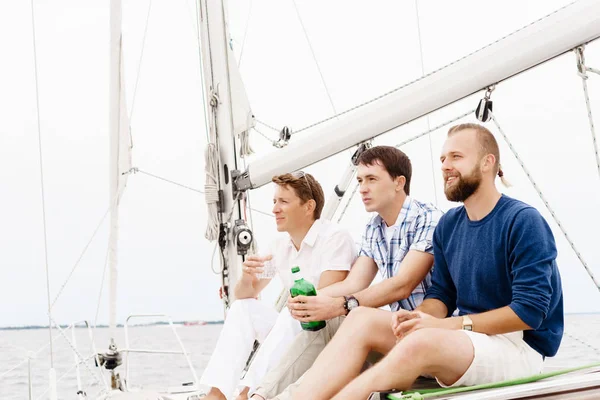 Glückliche Freunde sitzen zusammen auf dem Deck einer Jacht und trinken — Stockfoto