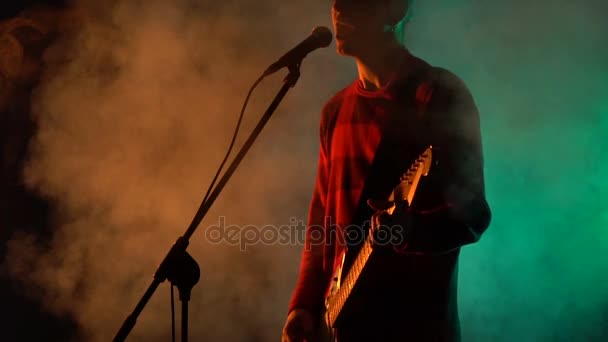 Хіпстер грає на гітарі і співає на сцені в диму. Повільний рух. Музика, звук, гурт, концепція . — стокове відео