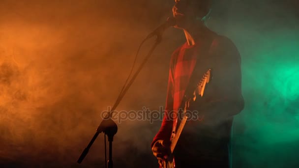 Hipster chico toca la guitarra en el escenario en el humo . — Vídeo de stock